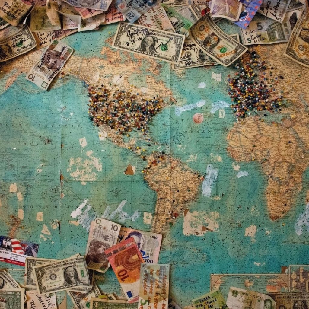 World map with scattered currency, symbolising budget-conscious travel planning for educational trips.