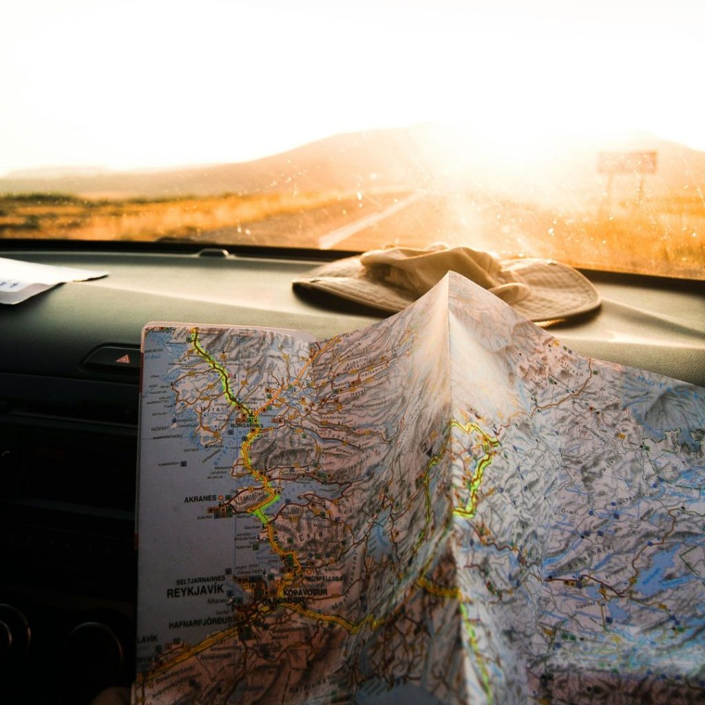 A road map spread out on a car dashboard with a hat placed nearby, illuminated by sunlight, symbolising an educational travel journey or road trip planning.