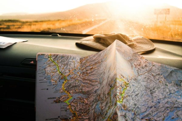 A road map spread out on a car dashboard with a hat placed nearby, illuminated by sunlight, symbolising an educational travel journey or road trip planning.