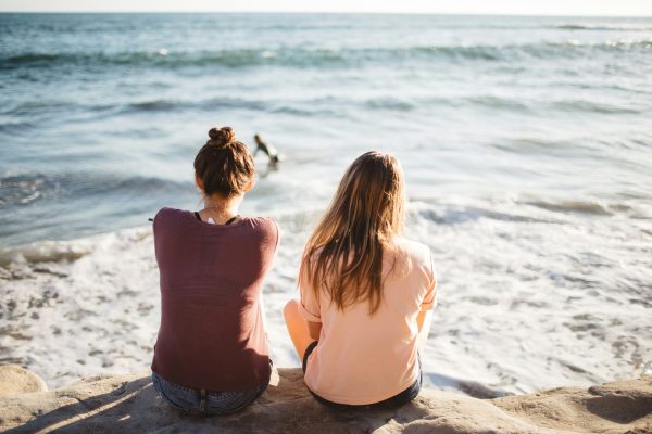 Two people sitting on the beach, facing the ocean, reflecting and relaxing.